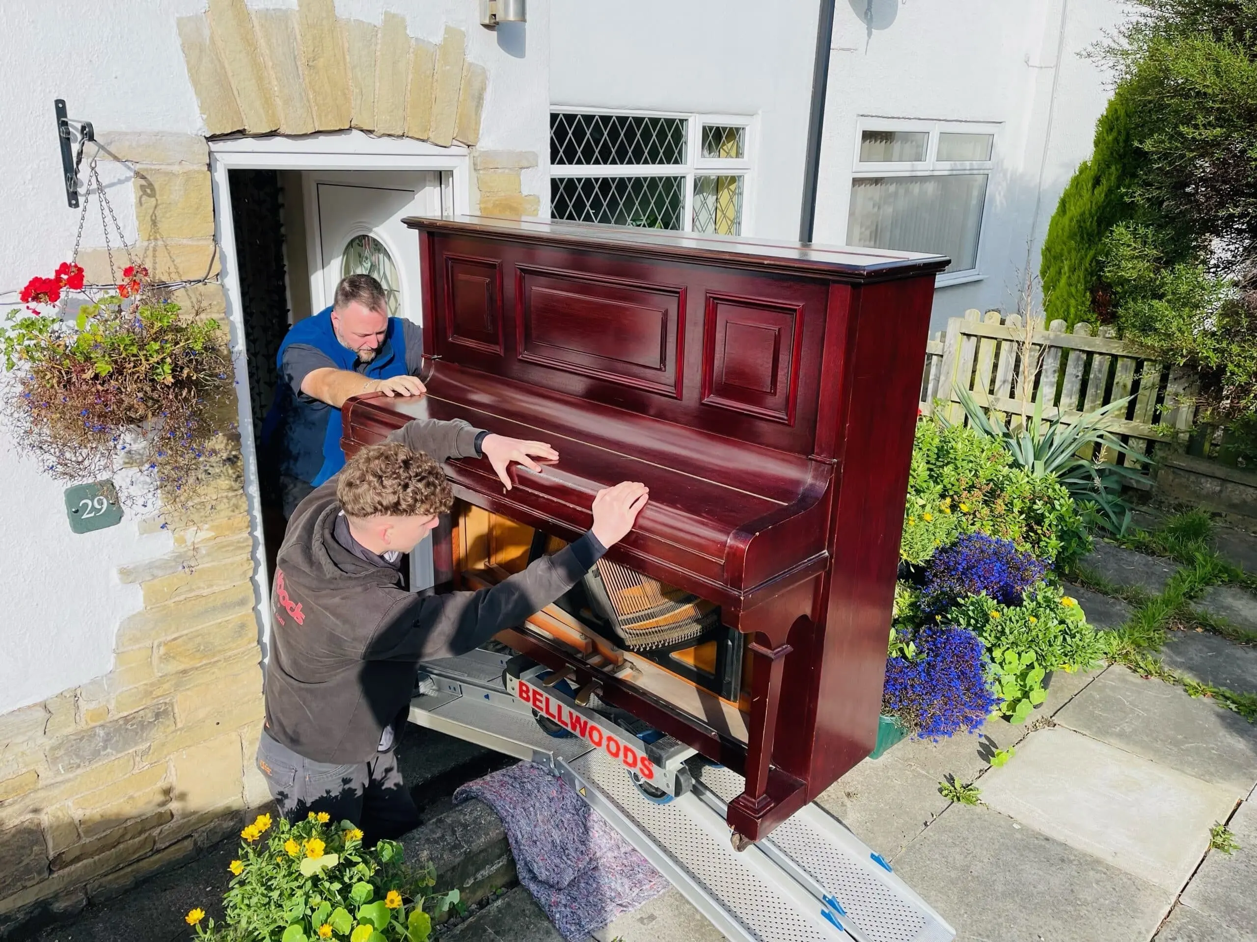We Move You crew easing an upright piano out of a stone cottage doorway